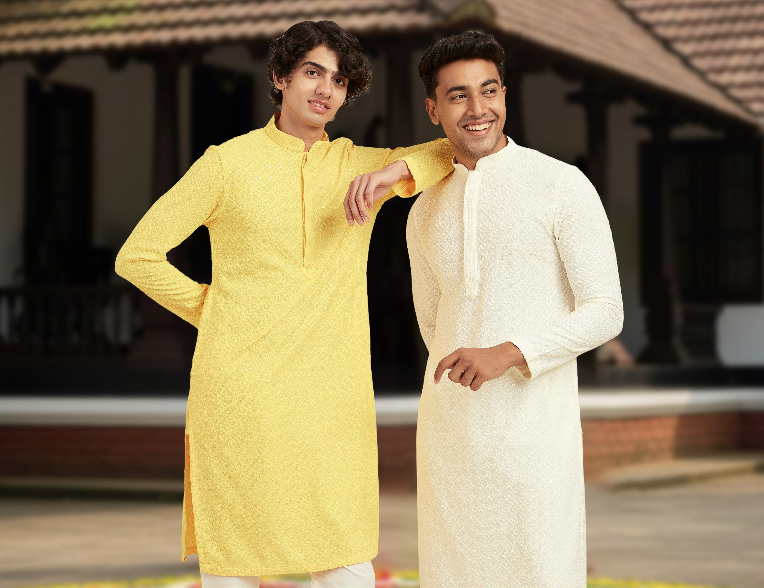 Men in yellow and white kurta pajamas posing in front of a traditional house for Onam celebration